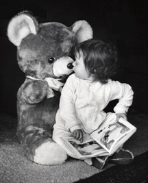 Photograph of toddler reading to stuffed bear